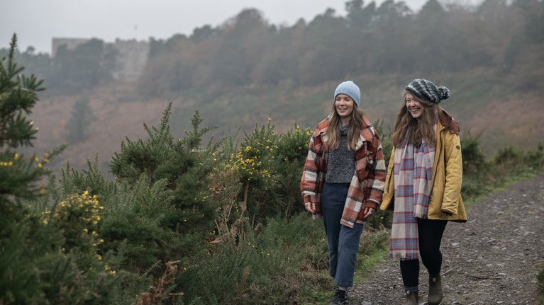 Visitors taking the Hunter's Path along the top of the Teign Gorge down towards Fingle Bridge with Castle Drogo in the background.